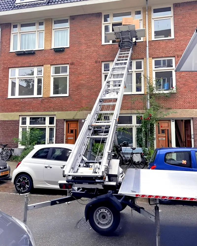 Verhuislift 4 highland-logistics.nl Professionele verhuislift in gebruik bij een typische Amsterdamse portiekwoning, perfect voor verhuizingen naar hogere verdiepingen zonder trappen te gebruiken